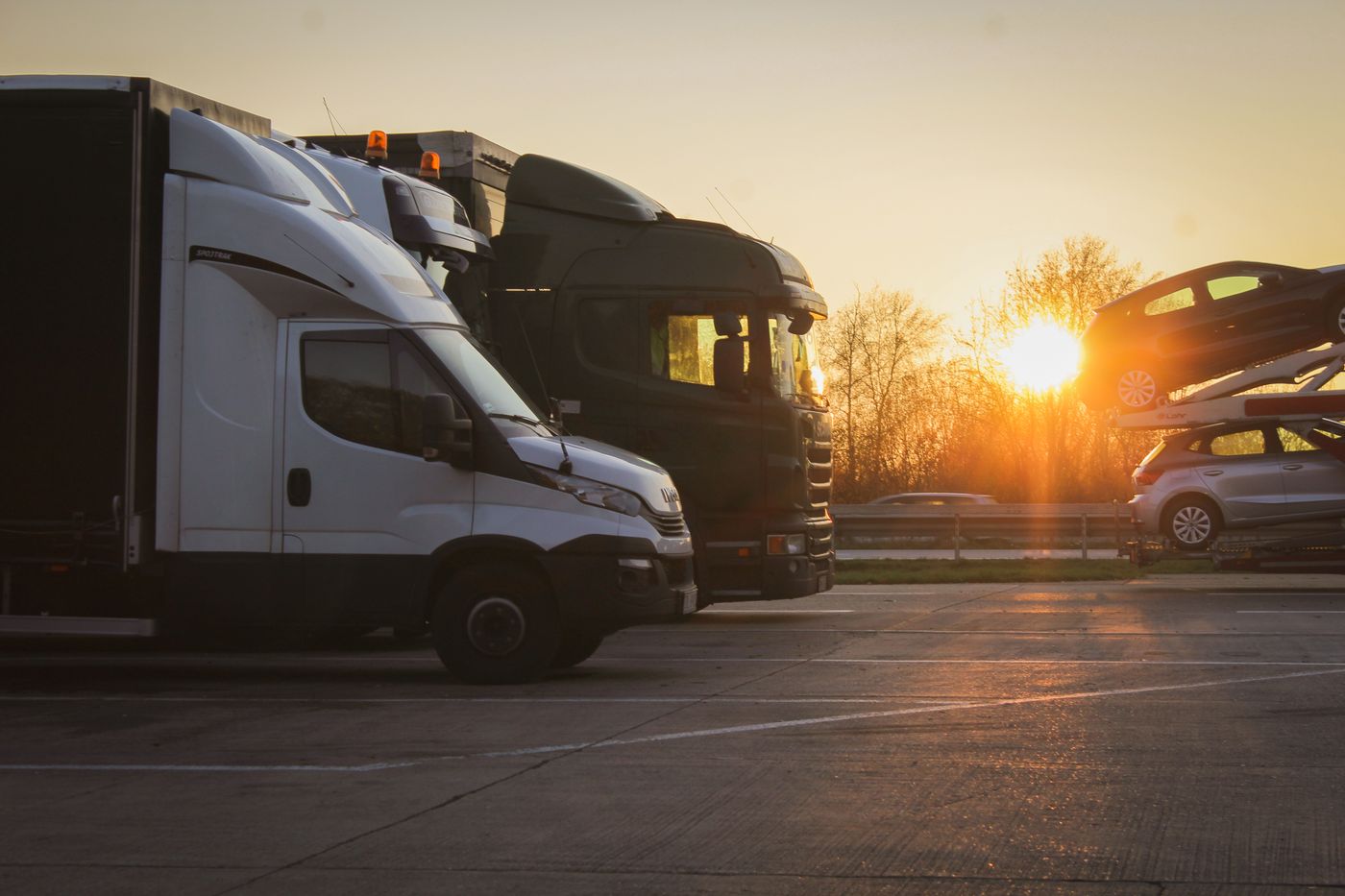 Camiones y camionetas de carga formados en un patio, con el sol bajo de la primera hora