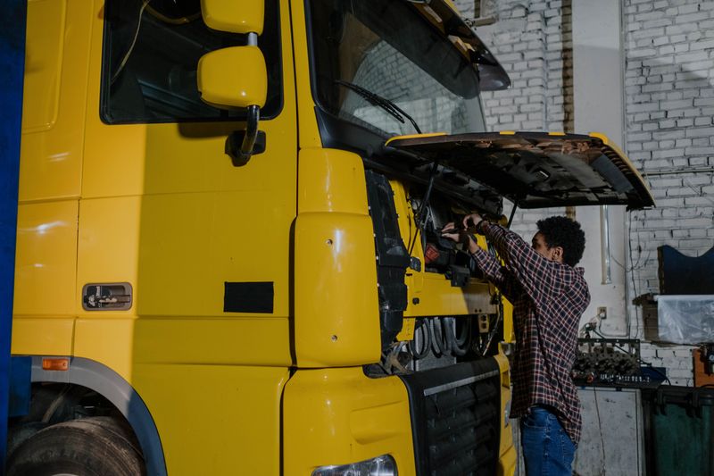 Un mecánico trabaja en el motor de un camión con el cofre abierto, dentro de un taller